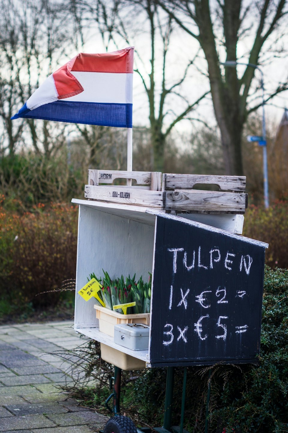 Zelfbedieningsbloemenkraam met tulpen en Nederlandse vlag.